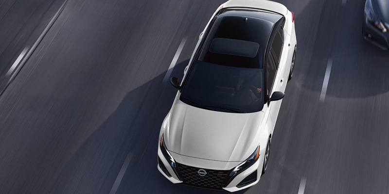 White Nissan Altima with a black roof driving on a highway
