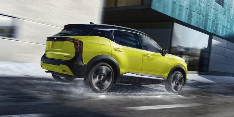 A bright yellow Nissan Kicks driving on a wet, slushy winter road next to a building.