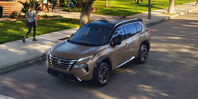 Tan Nissan Rogue parked on a city street with pedestrians walking in a nearby park.